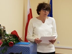 Fotografia kolorowa, na której widać Alinę Strugała, jak wygłasza przemówienie w związku ze swoim odejściem na emeryturę. Z boku widoczne kwiaty oraz upominki.