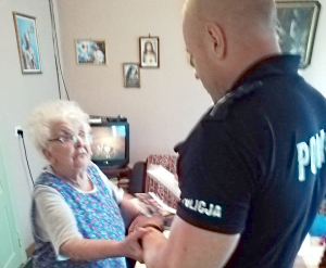 Fotografia kolorowa - policjant wita się ze starszą panią w jej domu