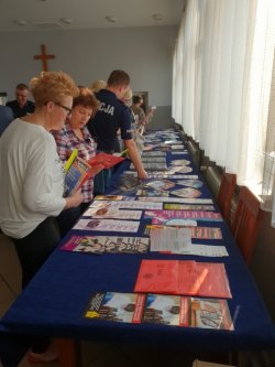 Fotografia kolorowa przedstawiająca gości, uczestniczących w debacie, którzy oglądają materiały profilaktyczne zaprezentowane podczas spotkania.