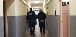 zdjęcie w kolorze - policjant prowadzi zatrzymanego